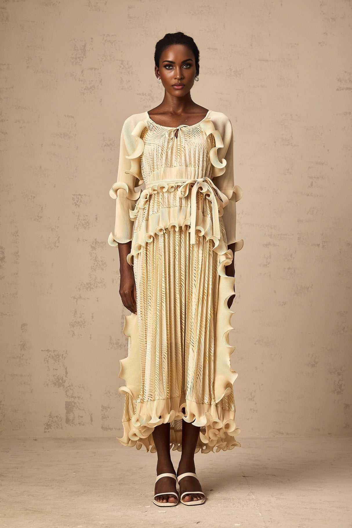 Woman wearing a neutral toned midi dress with ruffled details and gold accents standing in a relaxed pose