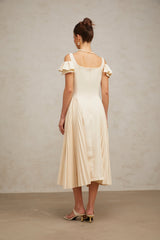 Woman wearing a neutralcolored pleated midi dress with a flared skirt and fitted bodice standing in a relaxed pose