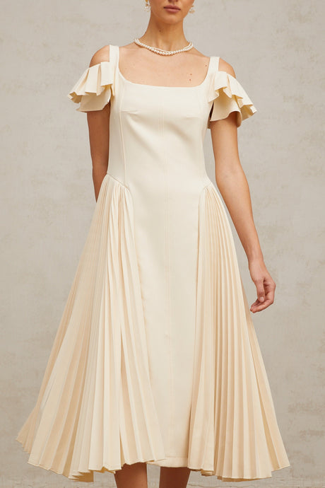 Woman wearing a neutralcolored pleated midi dress with flared skirt and short sleeves standing in front of plain background