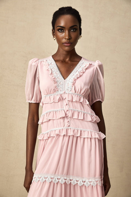 Woman wearing a pink midi dress with ruffled tiers and short sleeves standing against a plain background