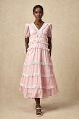 Woman wearing a pink midi dress with ruffled tiers and sleeveless design standing against a plain background