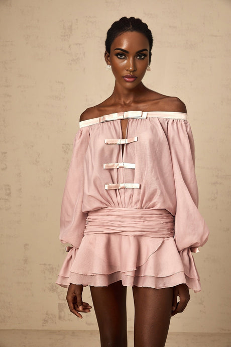 Woman wearing a pink offshoulder mini dress with bow detail and ruffled hem