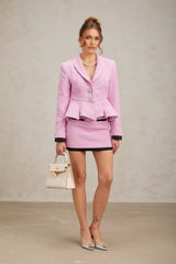 Woman wearing a pink tweed matching set consisting of a top and skirt standing against a plain background