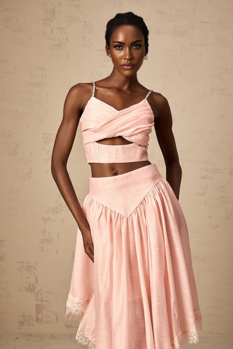 Woman wearing a pink two piece outfit consisting of an asymmetric ruffled top and matching skirt