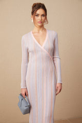 Woman wearing a pleated knit midi dress with V neckline in a light color standing against a neutral background