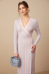 Woman wearing a pleated knit midi dress with V neckline in a soft color standing against a plain background
