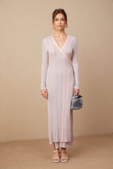 Woman wearing a pleated knit midi dress with V neckline in soft color standing against neutral background
