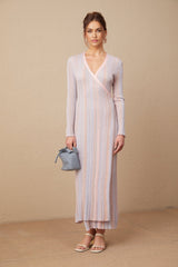 Woman wearing a pleated knit midi dress with Vneck in pale color standing against neutral background