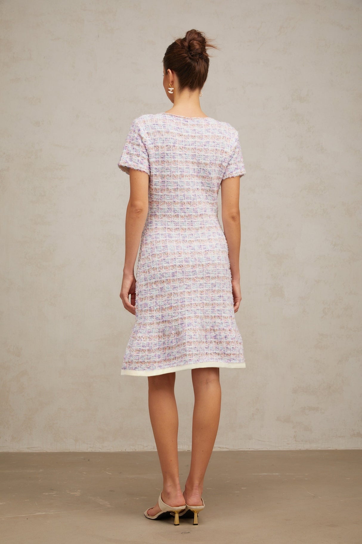 Woman wearing a purple checked knit midi dress with long sleeves and a fitted silhouette standing against a plain background