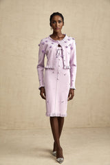 Woman wearing a purple knitted cardigan over a matching dress with faux flower embellishments on both pieces