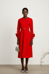 Woman wearing a red long sleeve dress with floral pattern standing against a plain background