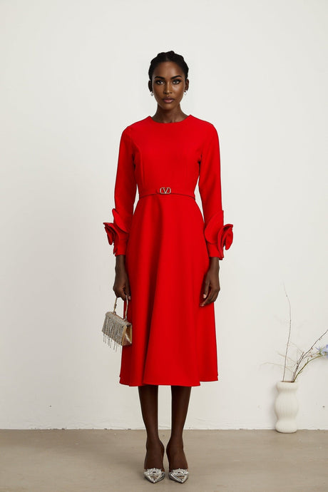 Woman wearing a red long sleeve dress with floral pattern standing against a plain background