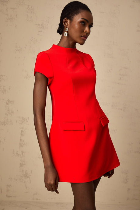 Woman wearing a red mini dress with cap sleeves standing against a plain background