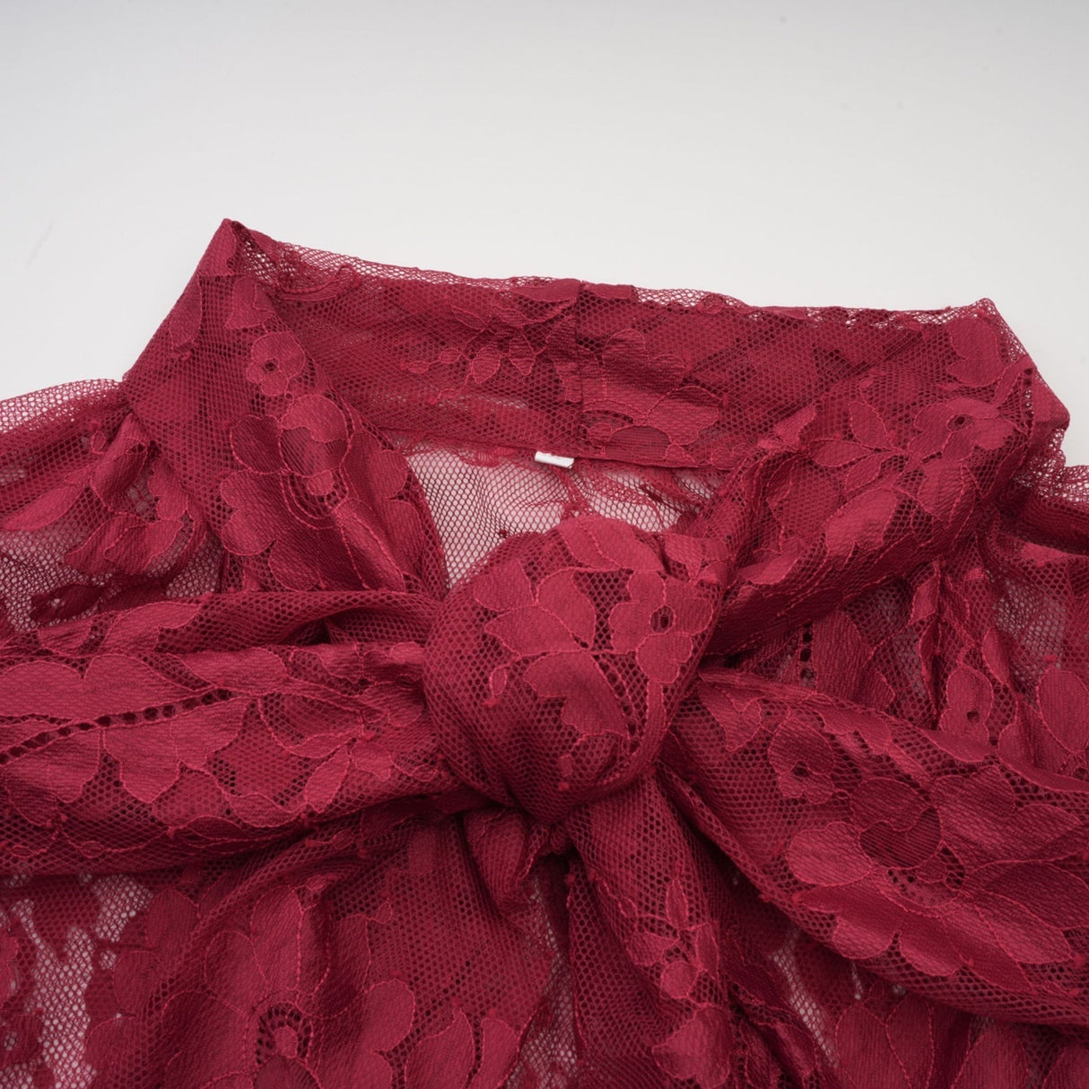 Woman wearing a red oversize dress made of chantilly lace standing against a plain background