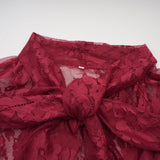 Woman wearing a red oversize dress made of chantilly lace standing against a plain background