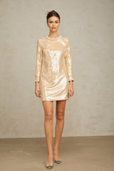 Woman wearing a short beige dress with faux pearl and sequin embellishments