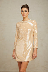 Woman wearing a short beige dress with faux pearl and sequin embellishments