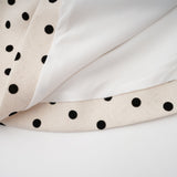 Woman wearing a short beige dress with white polka dots and puff sleeves standing against a plain background