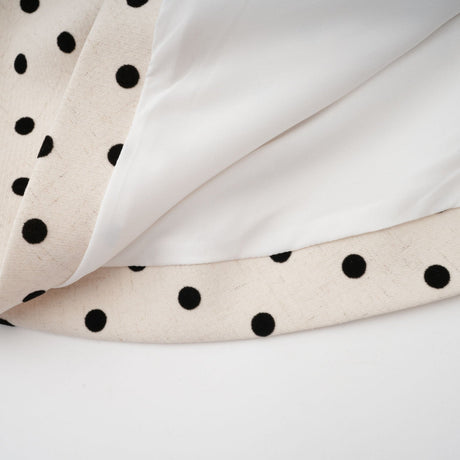 Woman wearing a short beige dress with white polka dots and puff sleeves standing against a plain background