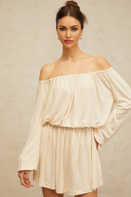 Woman wearing a short beige structured mini dress with a fitted silhouette and neutral tones standing against a plain background