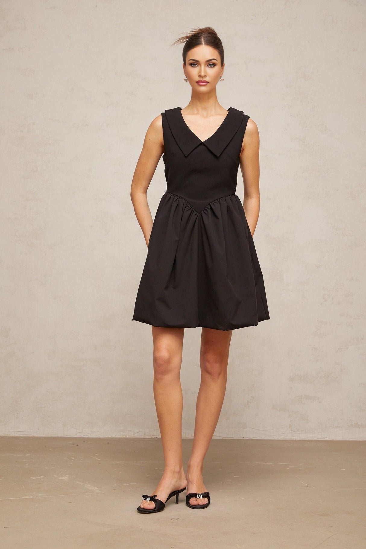 Woman wearing a short black dress with puff sleeves and a lapel collar