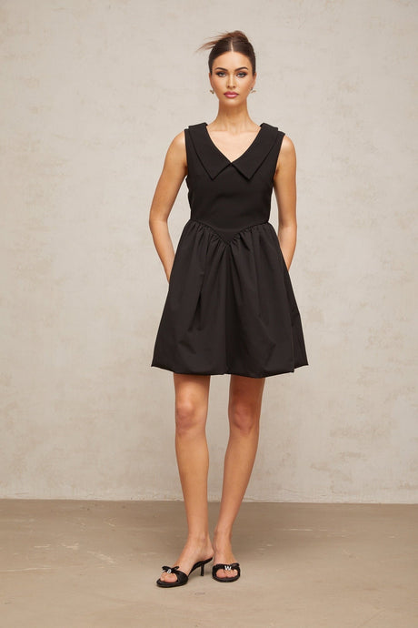 Woman wearing a short black dress with puff sleeves and a lapel collar