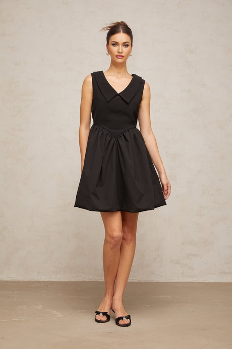 Woman wearing a short black dress with puffed sleeves and a lapel collar