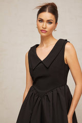 Woman wearing a short black dress with puffed sleeves and lapel detail