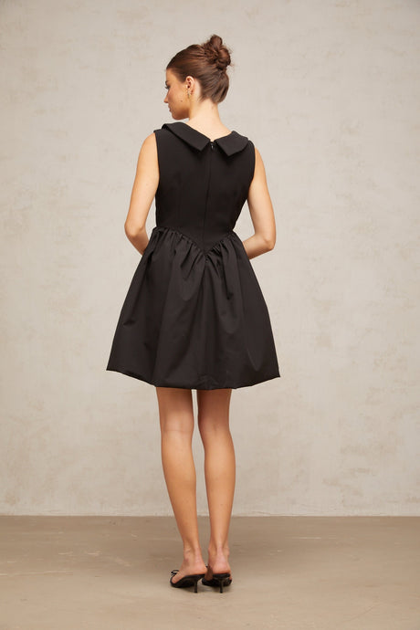 Woman wearing a short black dress with puffy sleeves and lapel collar