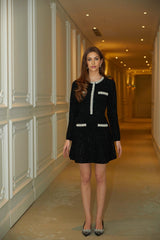 Woman wearing a short black knit dress with crystal sequin embellishments standing in a neutral pose
