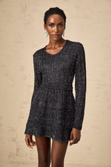 Woman wearing a short black knitted dress with allover sequin embellishment and form fitting silhouette