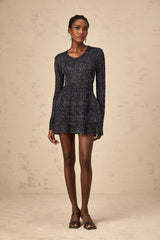 Woman wearing a short black knitted dress with sequin embellishments form fitting silhouette and mini length