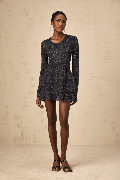 Woman wearing a short black knitted dress with sequin embellishments form fitting silhouette and mini length