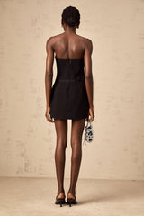 Woman wearing a short black mini dress with puffy sleeves and a large bow detail at the neckline