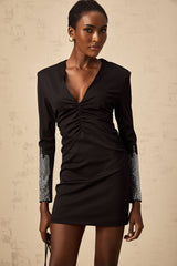 Woman wearing a short black mini dress with rhinestone embellishments and gathered fabric detailing