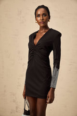 Woman wearing a short black mini dress with rhinestone embellishments and gathered fabric details