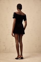Woman wearing a short black velvet dress with sparkly embellishments and thin straps