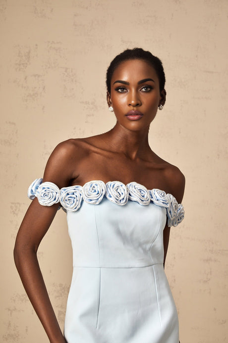 Woman wearing a short blue dress with floral applique details standing against a plain background