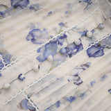 Woman wearing a short flared chiffon dress with a floral print pattern in pastel colors against a plain background