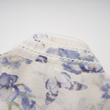 Woman wearing a short flared chiffon dress with floral print pattern in light colors standing against neutral background