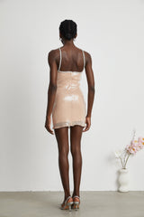 Woman wearing a short floral dress with sequin embellishments in a shimmering design against a plain background