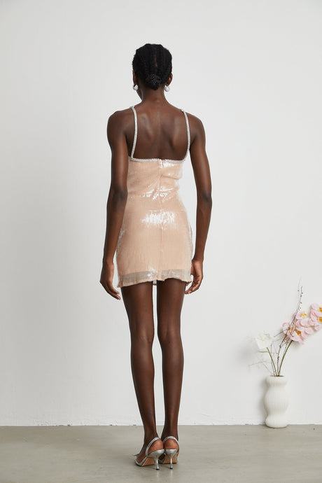 Woman wearing a short floral dress with sequin embellishments in a shimmering design against a plain background