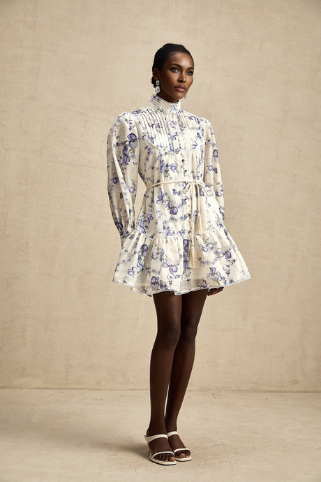 Woman wearing a short floral print chiffon dress with flared skirt and flowing sleeves in soft pastel colors against a plain background