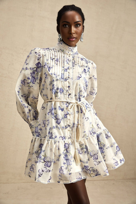 Woman wearing a short floral print dress with flared skirt and chiffon fabric in light colors against a plain background