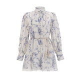 Woman wearing a short floral print dress with flared sleeves and a flowy chiffon fabric in light colors against a plain background