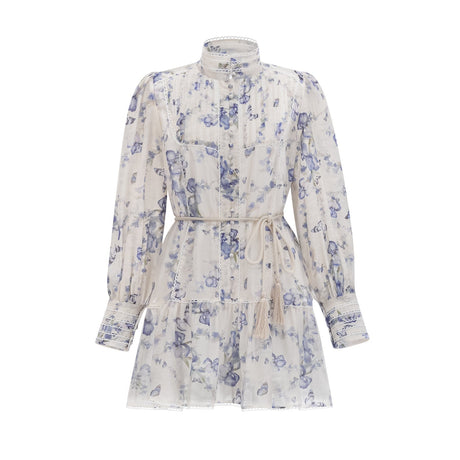 Woman wearing a short floral print dress with flared sleeves and a flowy chiffon fabric in light colors against a plain background