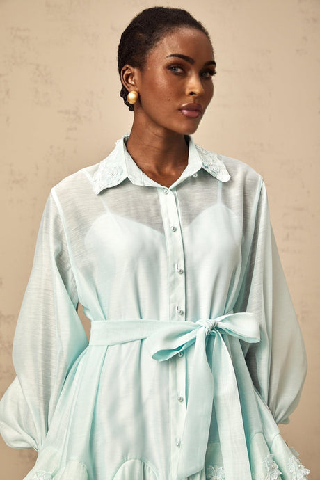 Woman wearing a short green dress with lace panels and a shirt collar standing against a plain background