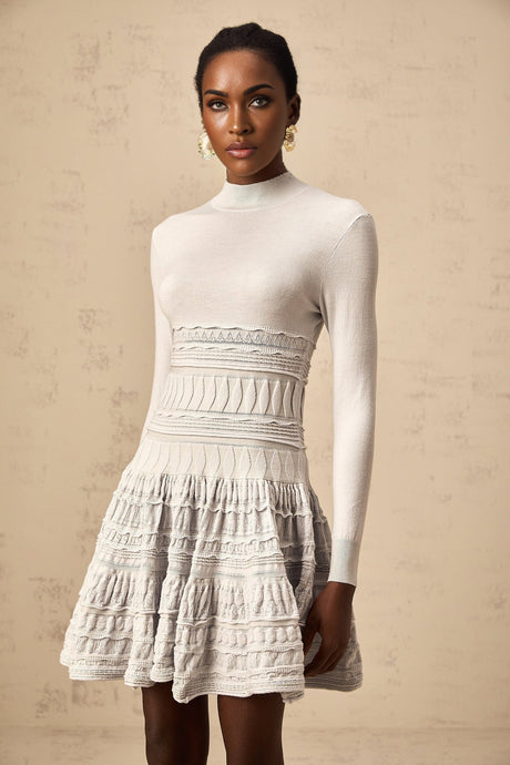 Woman wearing a short grey dress with ruffled details and ribbed texture standing against a plain background