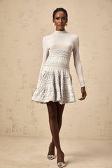 Woman wearing a short grey dress with ruffled details and ribbed texture standing against a plain background