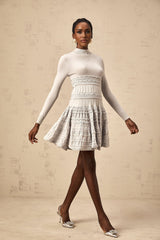 Woman wearing a short grey dress with ruffled details and ribbed texture standing against a plain background